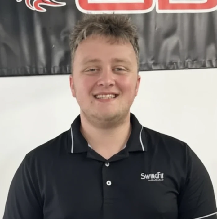 A young man with short hair smiles at the camera, wearing a black collared shirt with "SwingIt" logo. A black banner with red and white text hangs in the background.